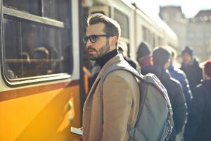 A stylish man with a backpack boards a tram in bustling Budapest, Hungary, during the day.